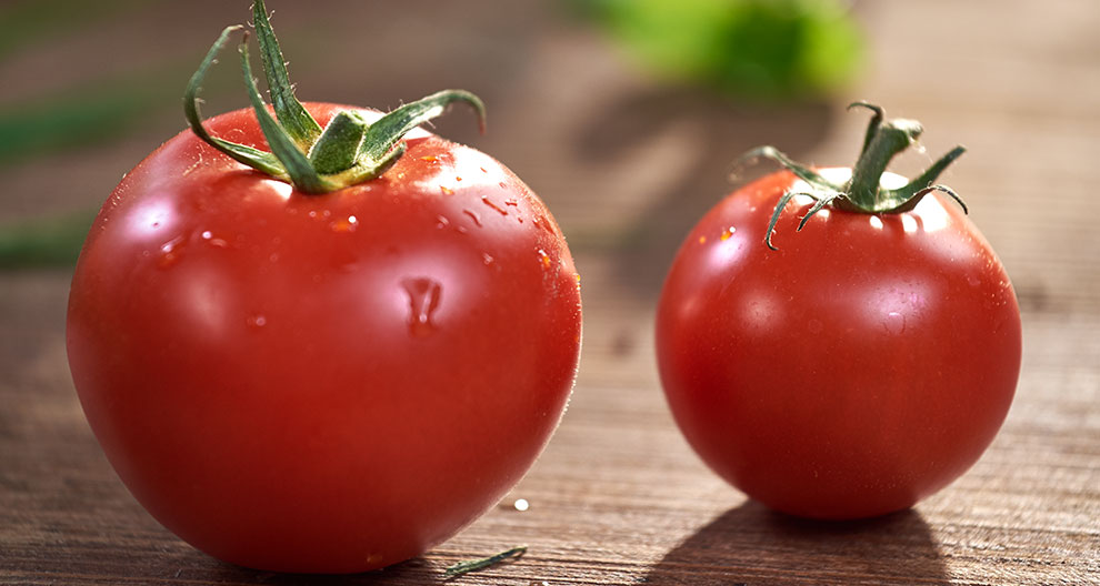 Two tomatoes with green stems are placed on a wooden surface.